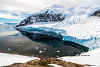 A sweeping Antarctic landscape featuring the towering ice cliffs of Neko Harbour reflected in calm, dark water under soft polar light.