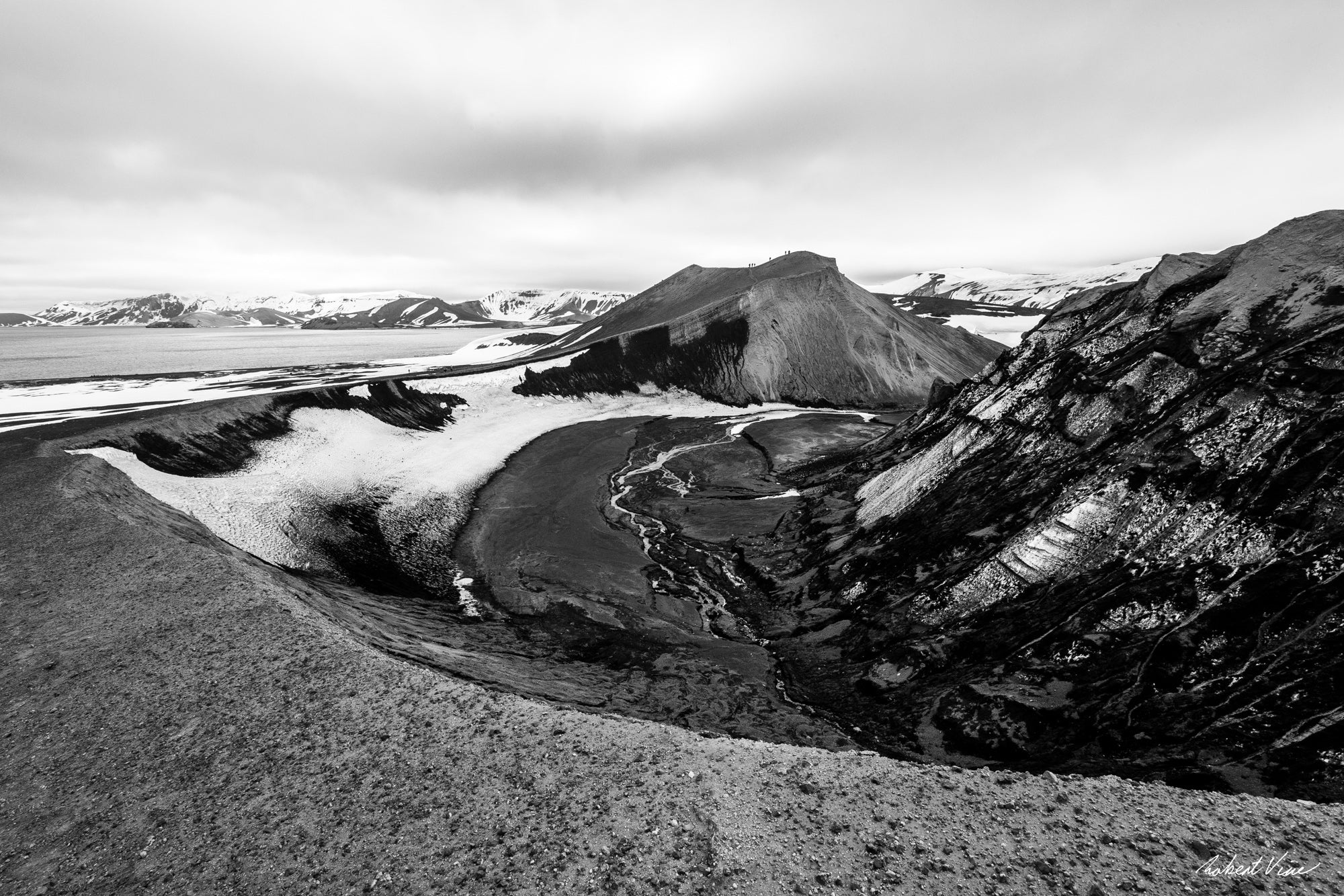 Black and white landscape photograph of Deception Island, Antarctica, showing volcanic slopes, glacial textures and winding meltwater channels.
