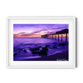 Fine art photograph of Catherine Hill Bay pier at sunset, with purple twilight tones reflecting across calm ocean waters and smooth rocks in the foreground. Landscape art print by Robert Vine.