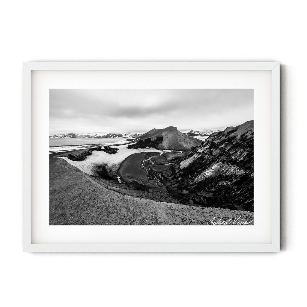 Black and white landscape photograph of Deception Island, Antarctica, showing volcanic slopes, glacial textures and winding meltwater channels.