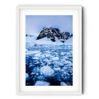 A dramatic Antarctic landscape at Paradise Bay featuring fractured sea ice, blue glacial water, and a snow-covered mountain rising into low cloud.