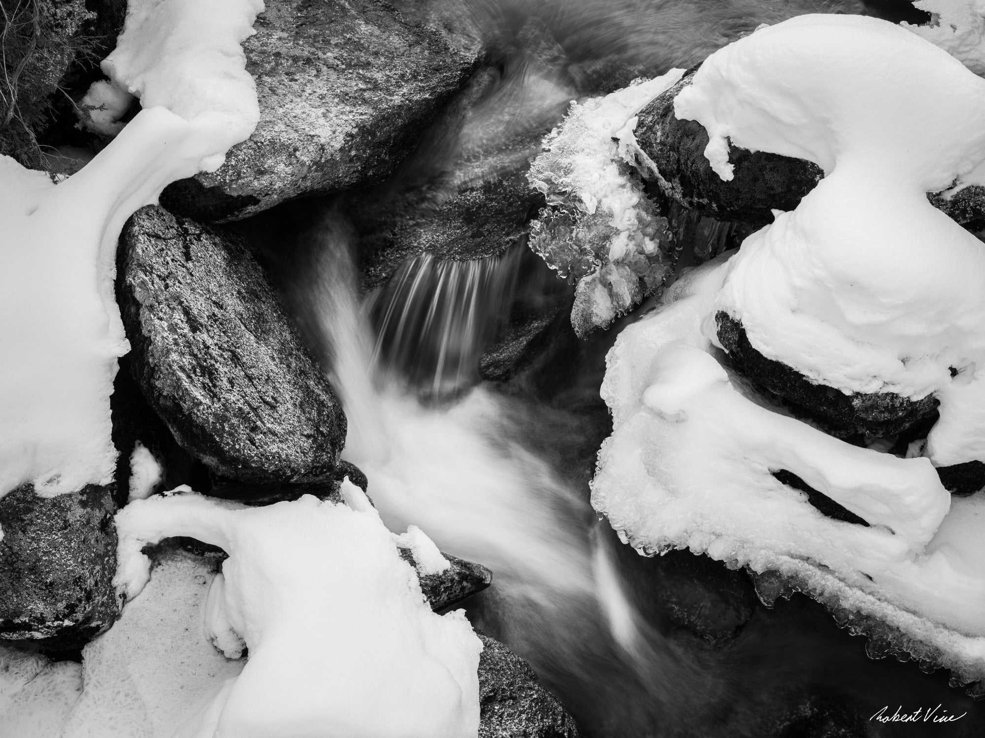 Black and white winter landscape art print of flowing water among snow-covered rocks — minimalist fine art photography for modern interiors.