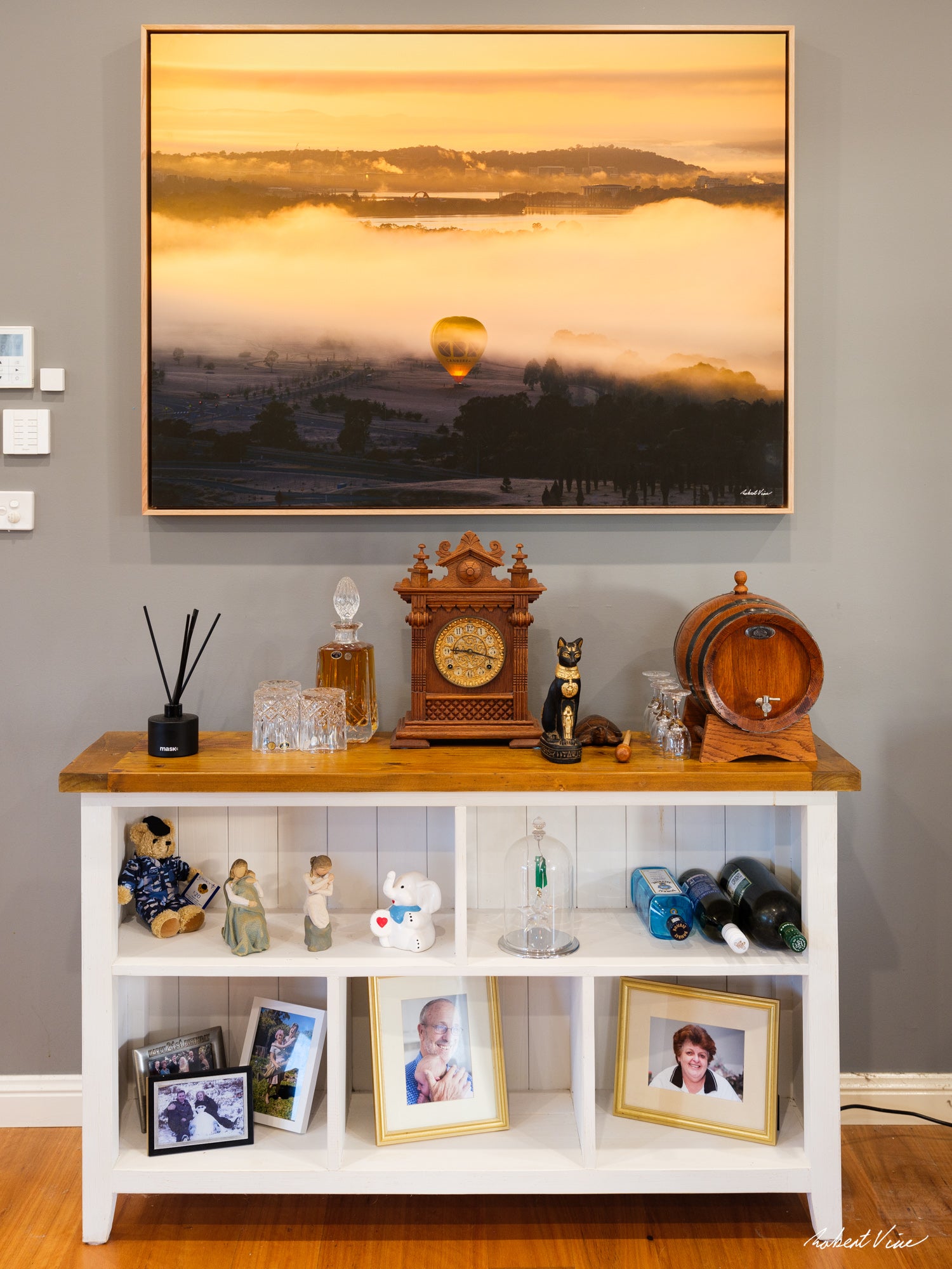 80x106cm float mount canvas print by Robert Vine featuring a hot air balloon rising through morning fog over Canberra, displayed in a contemporary home interior with a natural timber float frame.