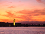 The National Carillon illuminated at sunrise on Lake Burley Griffin, Canberra, beneath vibrant orange and pink clouds reflected across calm morning waters.