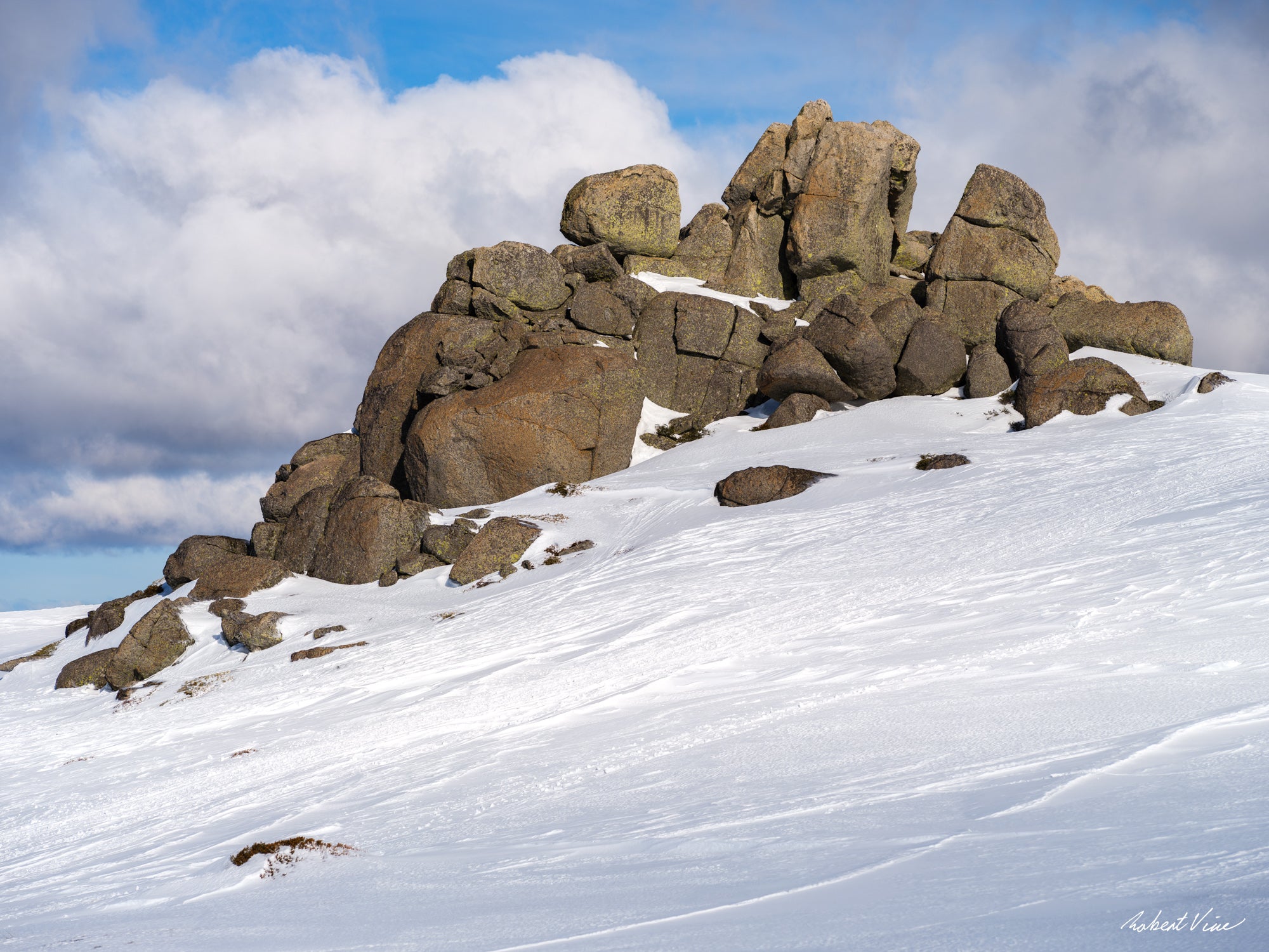 Snow-covered granite rock formation at the summit of Thredbo beneath dramatic alpine clouds in the Snowy Mountains, photographed by Robert Vine.