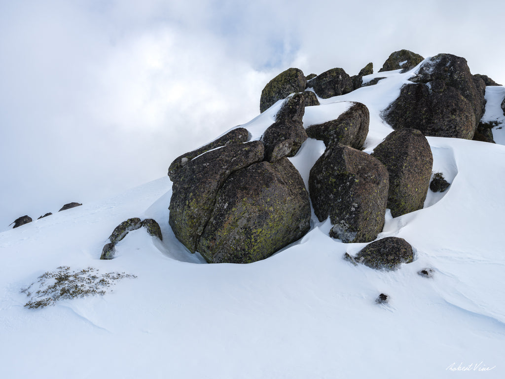 Snow-covered granite boulders rising from pristine alpine snow beneath a cloudy sky near Thredbo in the Snowy Mountains, photographed by Robert Vine.