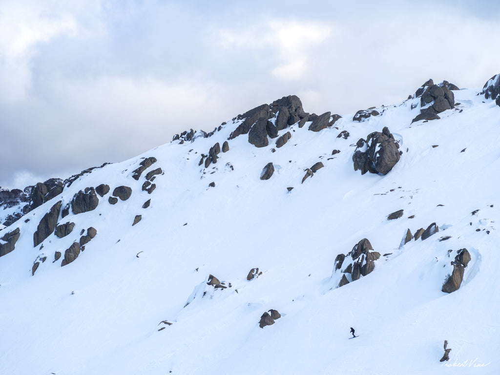 A lone skier descending beneath snow-covered granite cliffs at Thredbo in the Snowy Mountains, photographed by Australian landscape artist Robert Vine.