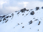 A lone skier descending beneath snow-covered granite cliffs at Thredbo in the Snowy Mountains, photographed by Australian landscape artist Robert Vine.