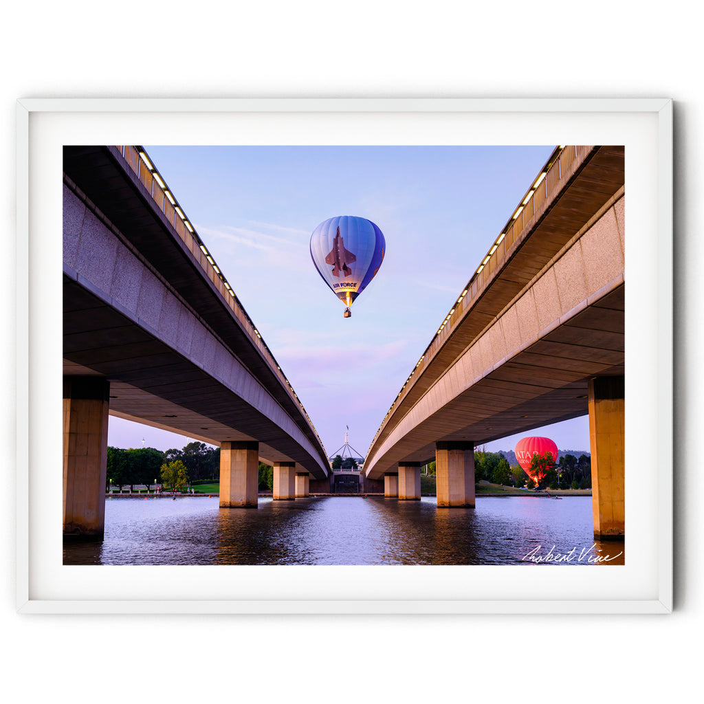 Framed print of the Air Force hot air balloon flying between Commonwealth Avenue Bridge spans with Parliament House in the background at dawn in Canberra.