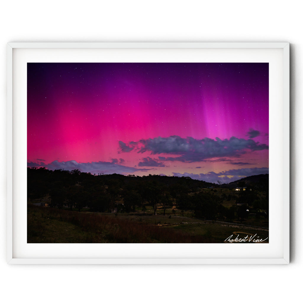 Framed landscape image of Aurora Australis glowing pink and purple over the hills of Royalla near Canberra beneath a star-filled night sky, photographed by Robert Vine.