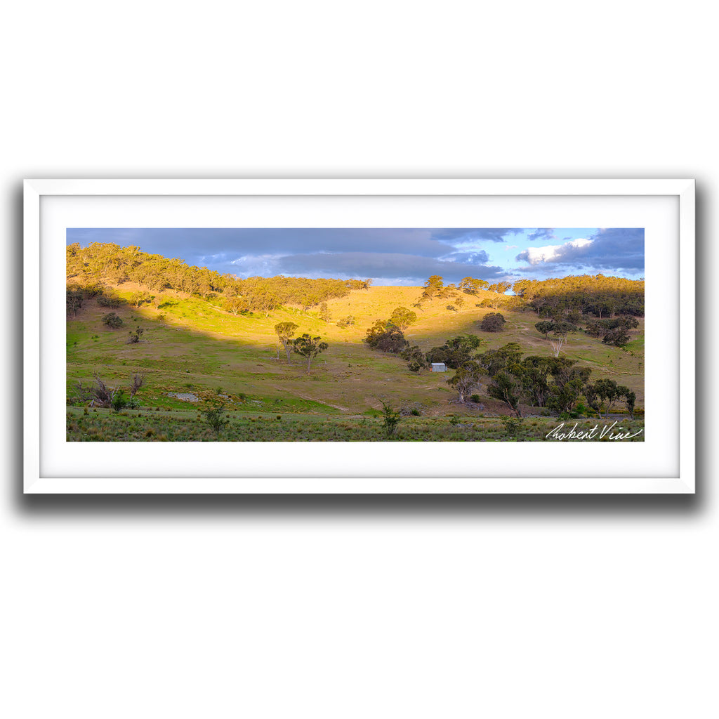 Framed print of Golden sunset light illuminating rolling hills and valleys near Burra beneath dramatic storm clouds, limited edition landscape art print by Robert Vine.
