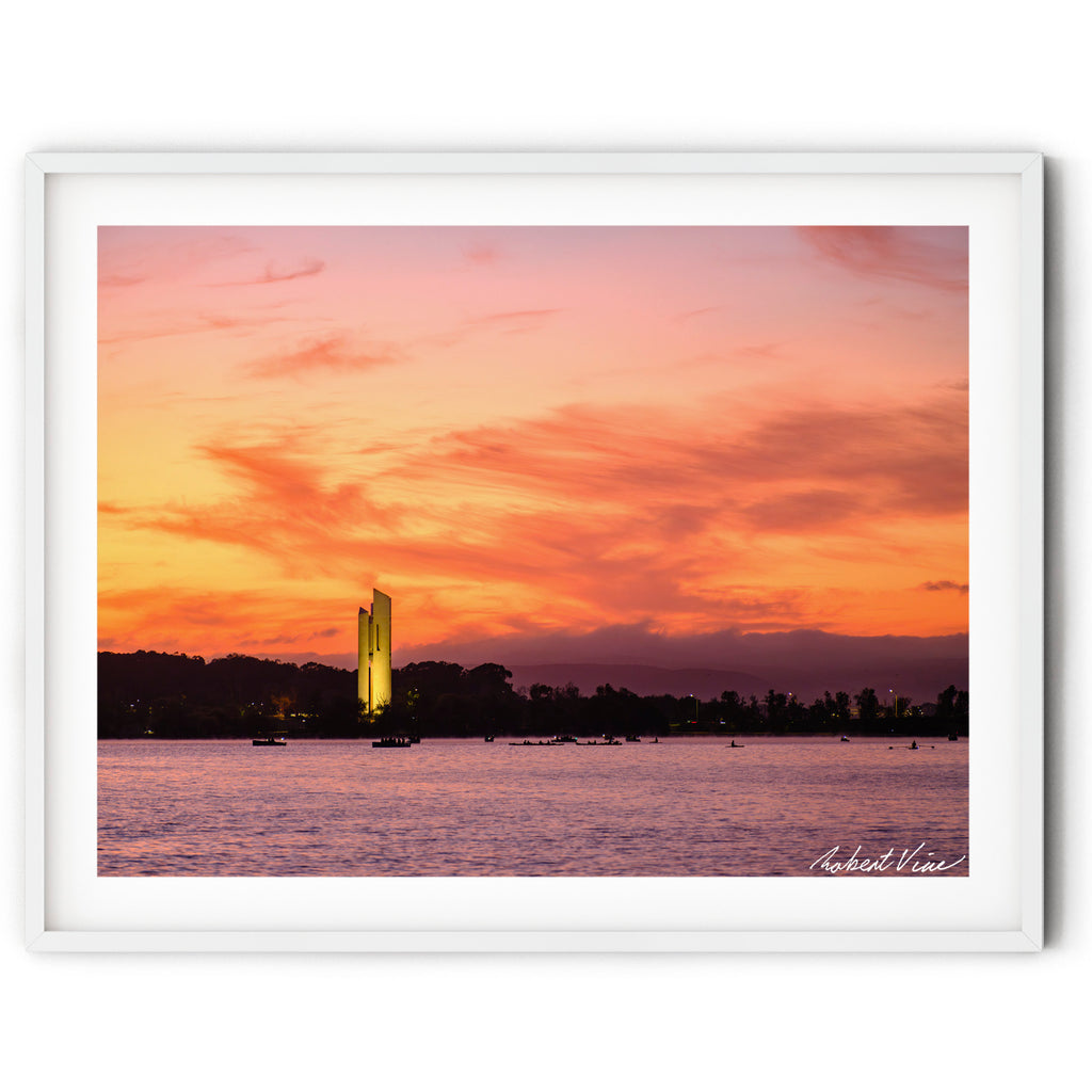 Framed print of The National Carillon illuminated at sunrise on Lake Burley Griffin, Canberra, beneath vibrant orange and pink clouds reflected across calm morning waters.