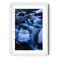 Long exposure photograph of the icy Thredbo River flowing between snow-covered granite boulders in the Australian Alps during winter.