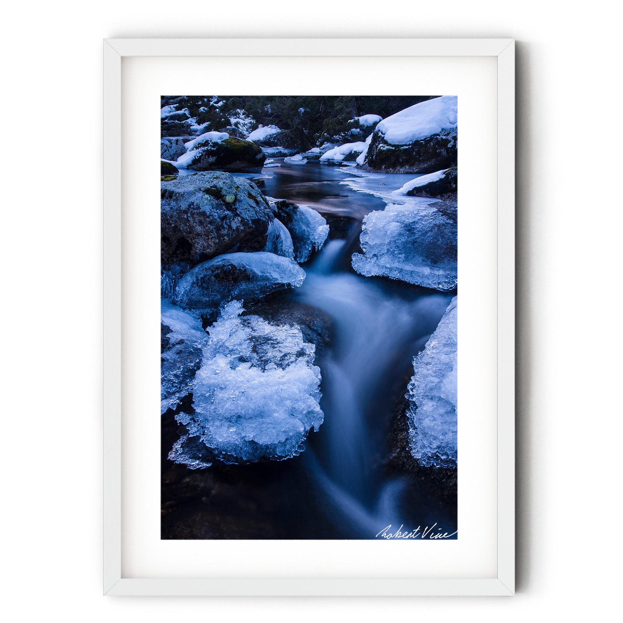 Long exposure photograph of the icy Thredbo River flowing between snow-covered granite boulders in the Australian Alps during winter.
