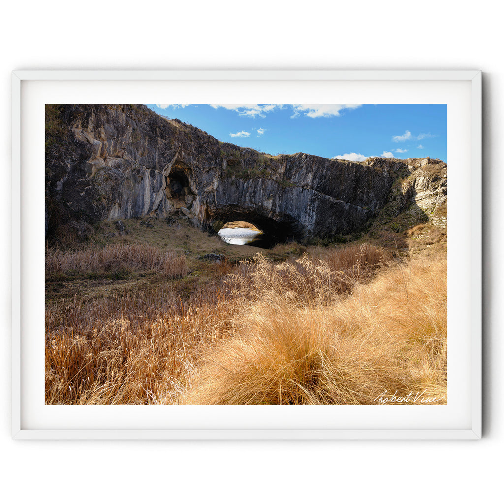 Framed print of an image of London Arch Bridge in Burra on a warm winter afternoon with golden grasses, rugged rock formations and blue sky, photographed by Robert Vine.