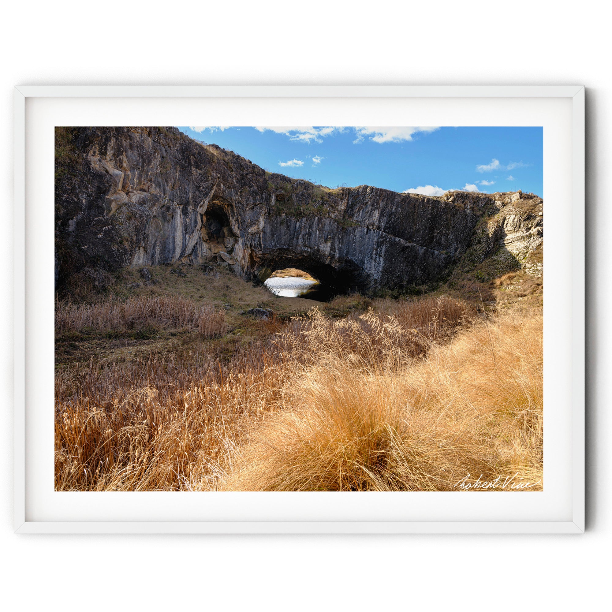 Framed print of an image of London Arch Bridge in Burra on a warm winter afternoon with golden grasses, rugged rock formations and blue sky, photographed by Robert Vine.