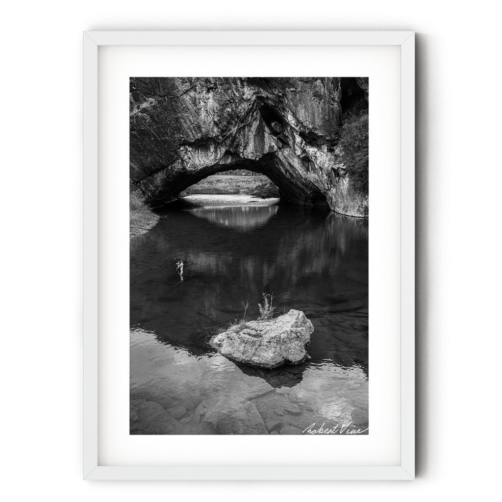 Frame print of Black and white photograph of London Bridge at Googong, NSW, reflected in calm water beneath the natural limestone arch by Robert Vine.