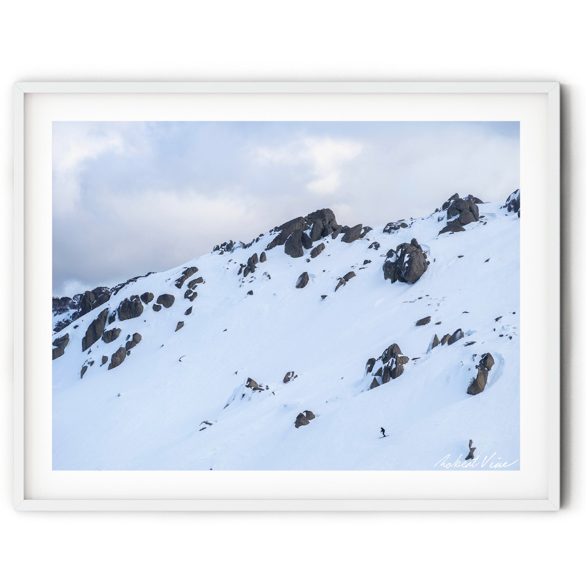 Framed wall art of a lone skier descending beneath snow-covered granite cliffs at Thredbo in the Snowy Mountains, photographed by Australian landscape artist Robert Vine.